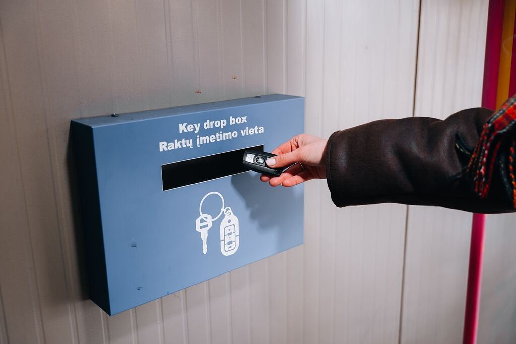 Ranka įmeta automobilio raktelius į mėlyną ADCParking raktų įmetimo dėžutę